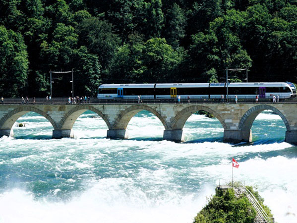 Een foto van trein rijdend op een spoorwegbrug met wandelaars in de nabije omgeving van de Rijnwatervallen
